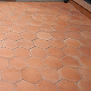 A rustic floor or patio covered in handmade hexagon terracotta tiles laid in a classic honeycomb pattern, showing their warm, natural color.