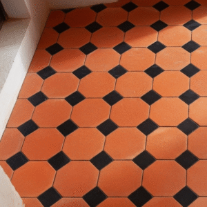 A close-up of a classic Octagon and Bouchon terracotta tile floor, featuring warm orange octagons and contrasting dark square bouchons.