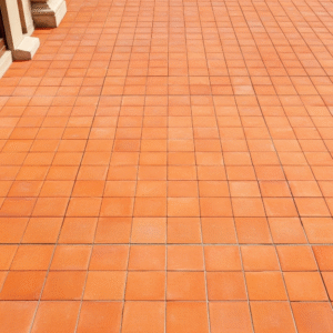A sunlit outdoor patio floor paved with square 10x10 cm Moroccan terracotta tiles laid in a clean, uniform grid pattern.