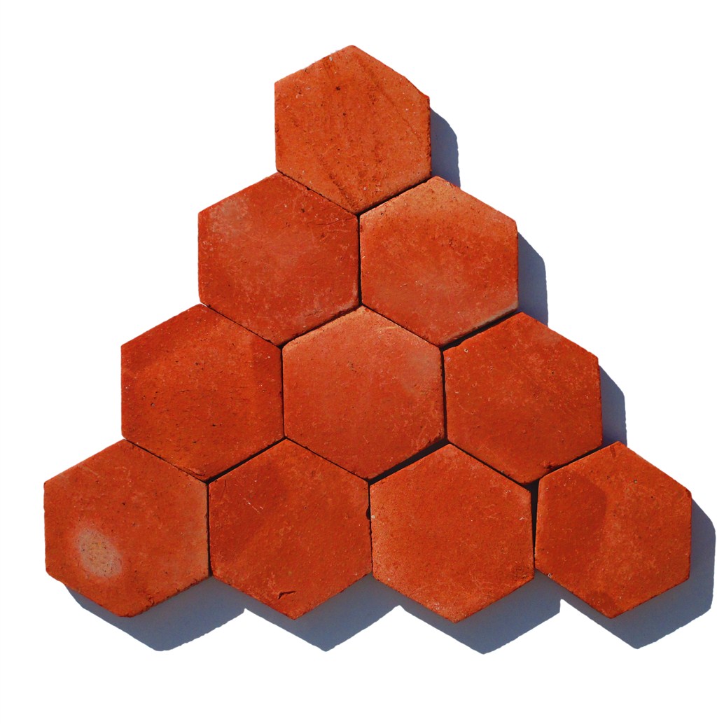 A triangular arrangement of handmade 10x10 cm hexagon terracotta tiles, showing the natural red clay color and rustic surface texture.